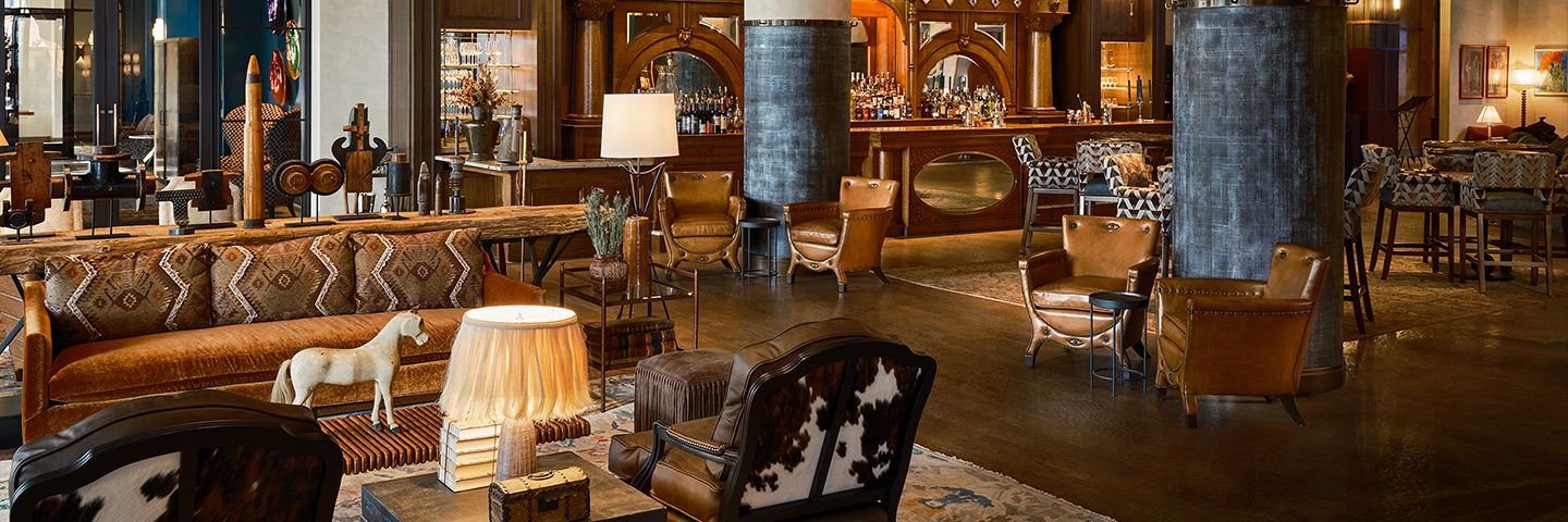 Elegant rustic hotel lounge featuring leather armchairs, a large wooden bar, and western-themed decor with warm lighting.