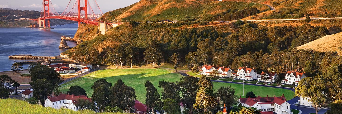 Golden Gate Bridge spanning the bay, viewed from a hillside with white houses, green fields, and rolling terrain.