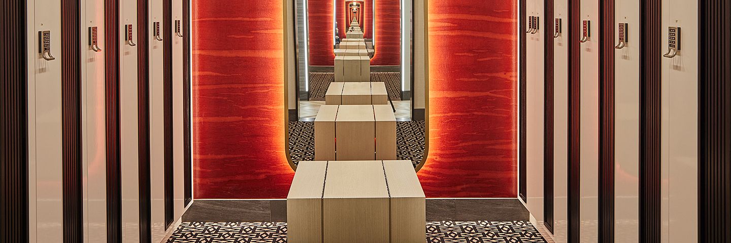 Modern locker room aisle with red walls and wooden benches reflected in an infinity mirror.