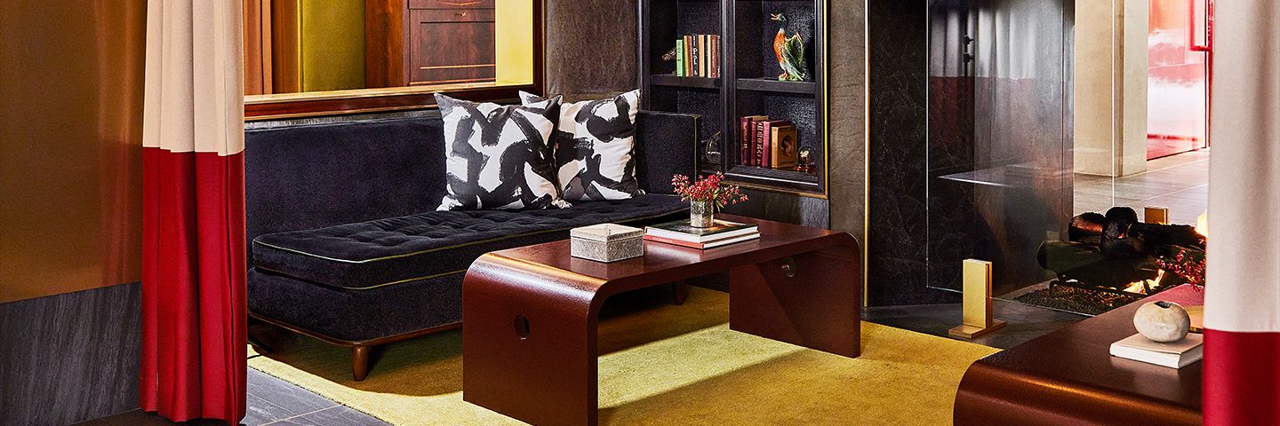 Modern lounge featuring a dark tufted sofa with patterned pillows, a curved wood coffee table, and a vibrant yellow rug.