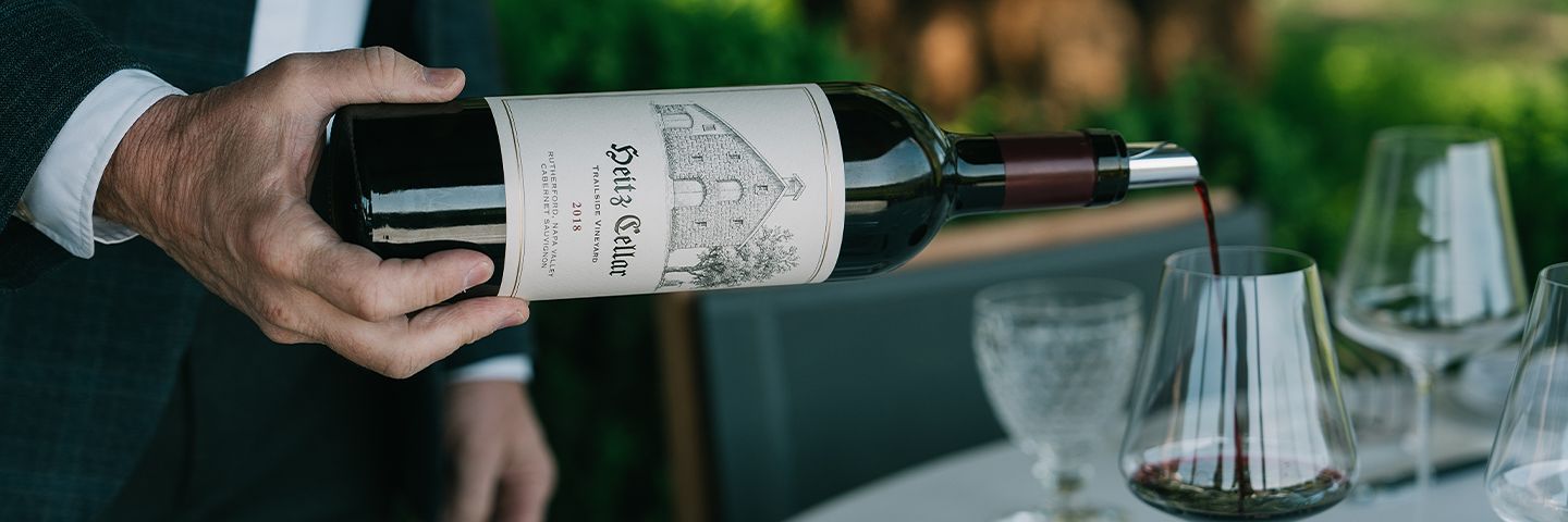 A person pours Heitz Cellar 2018 Cabernet Sauvignon into a glass at an outdoor table.
