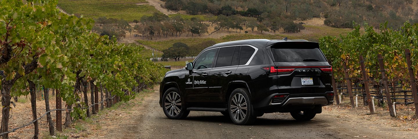 Black Lexus SUV with Heitz Cellar branding parked on a dirt road between vineyard rows.