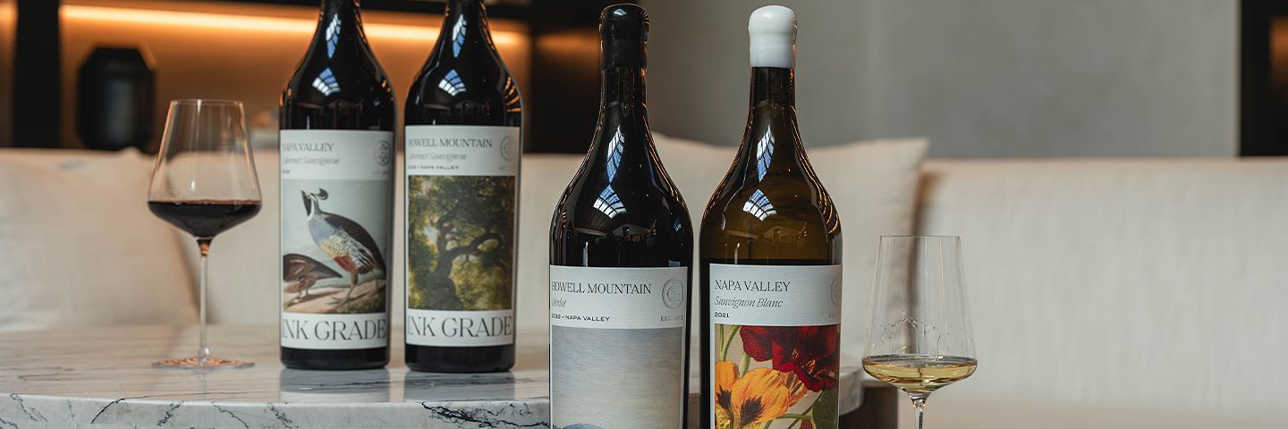 Ink Grade wine bottles with illustrated labels and glasses of red and white wine on marble tables.